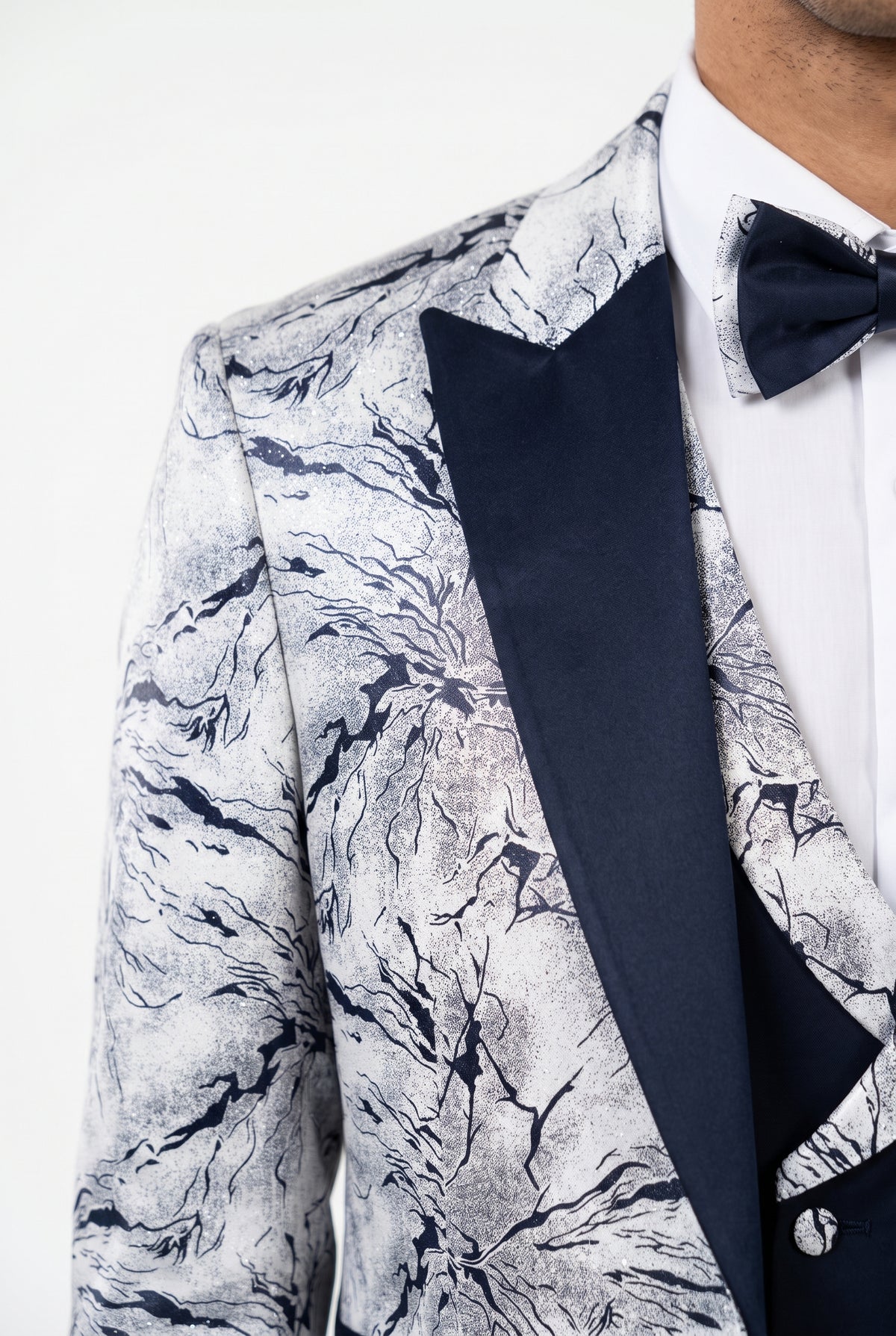 A close-up of a men's tuxedo jacket featuring a navy and white marble pattern on the body and a solid navy blue satin peak lapel, styled with a white dress shirt and a matching navy bow tie.