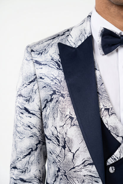 A close-up of a men's tuxedo jacket featuring a navy and white marble pattern on the body and a solid navy blue satin peak lapel, styled with a white dress shirt and a matching navy bow tie.