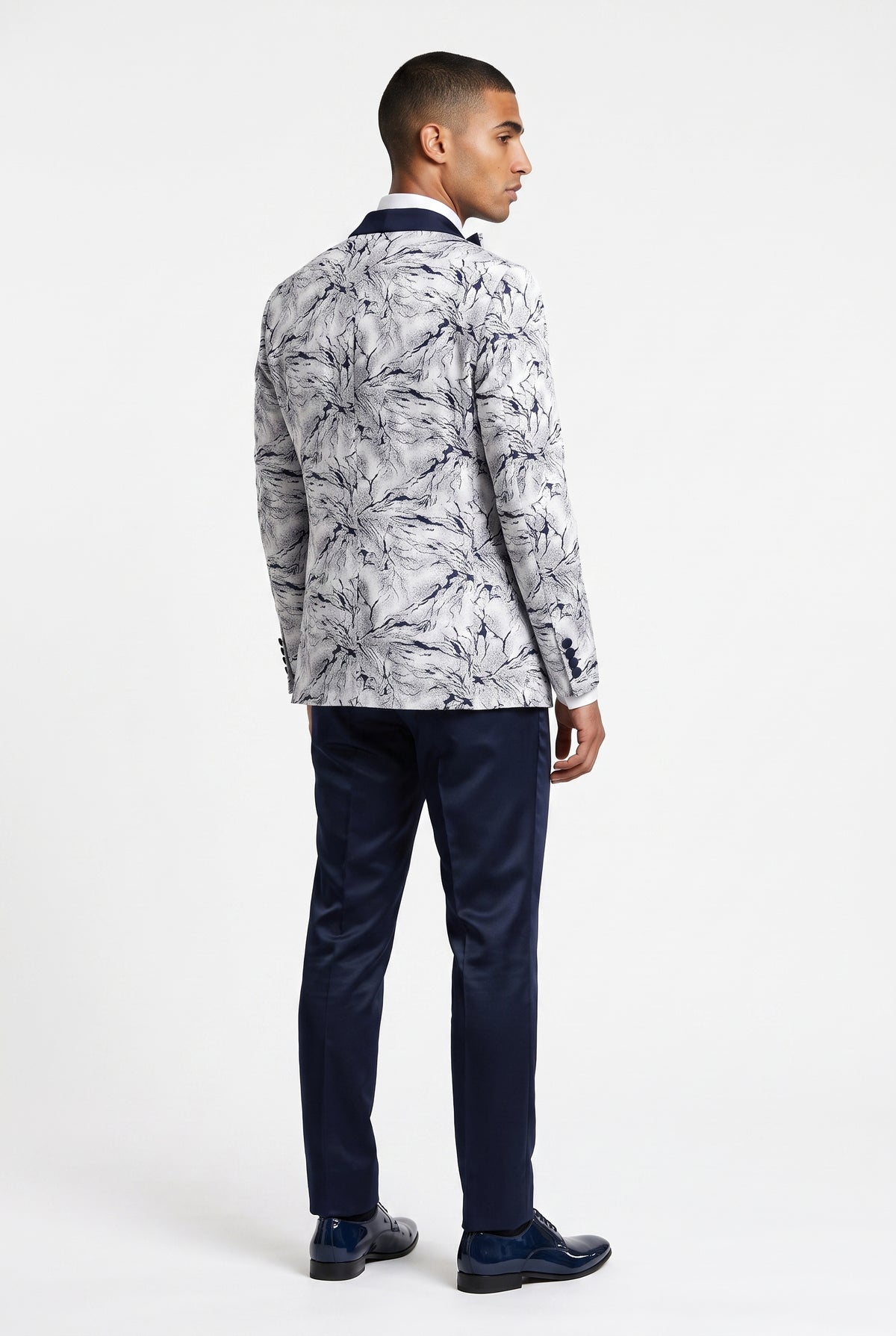 A man shown from the back wearing a white and navy print blazer, navy trousers, and navy dress shoes, photographed against a clean white studio background.